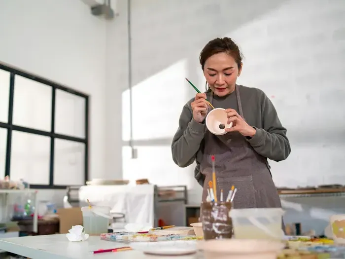 Artist painting a ceramic bowl in a bright studio, showing CityBiz World supporting creative local businesses